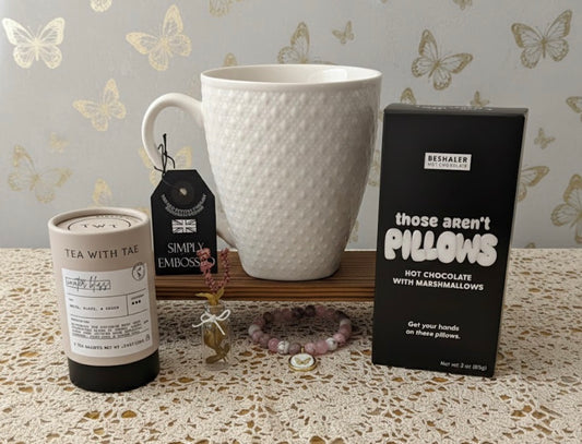 White textured mug, tea canister, and box of hot chocolate on a surface with decorative butterfly wallpaper.