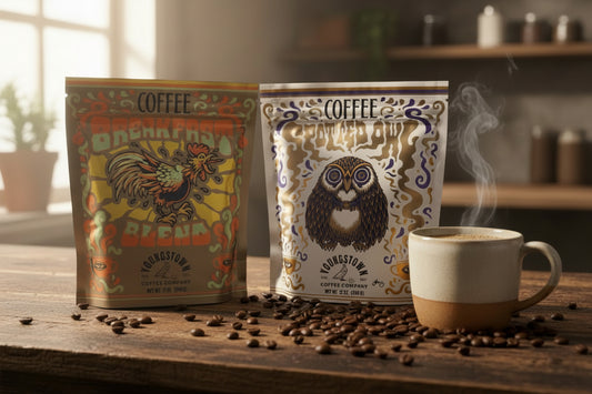 Two coffee packages and a steaming cup on a wooden table with coffee beans.